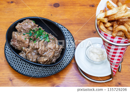 Hearty beef stew served in a decorative bowl alongside crispy fries and dipping sauce, showcasing a delicious culinary experience Hearty beef stew served in a decorative bowl alongside crispy fries and dipping sauce, showcasing a delicious culinary experience 135729206