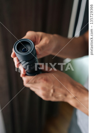 Vertical cropped shot of unrecognizable person holding monocular, observing, exploring, looking into distance, focusing on details with optical equipment, emphasizing vision and search. Vertical cropped shot of unrecognizable person holding monocular, observing, exploring, looking into distance, focusing on details with optical equipment, emphasizing vision and search. 135729366