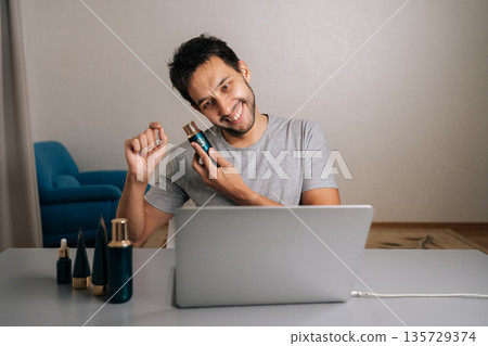 Positive bearded male vlogger creating skincare content online, reviewing beauty serum and making heart gesture with hands, connecting with audience about personal care and cosmetic products. 135729374