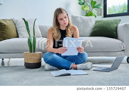 Serious sad young woman with business important papers in home interior Serious sad young woman with business important papers in home interior 135729487