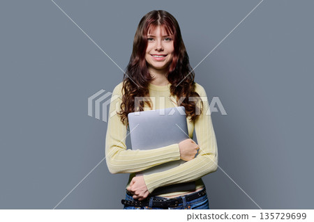 Portrait of beautiful girl teenage student holding laptop on gray background Portrait of beautiful girl teenage student holding laptop on gray background 135729699