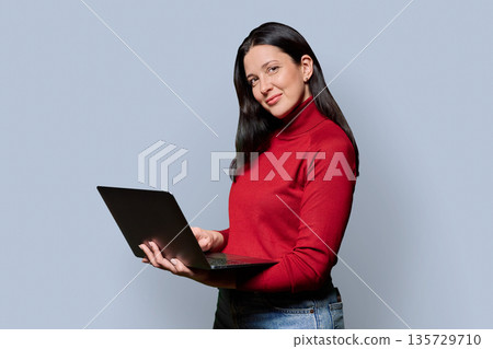 Portrait of successful middle-aged woman with laptop on grey background Portrait of successful middle-aged woman with laptop on grey background 135729710