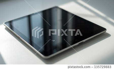 Black Tablet Rests on Wooden Table With Natural Light Creating Shadows in a Room Black Tablet Rests on Wooden Table With Natural Light Creating Shadows in a Room 135729883