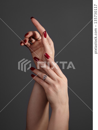 Beautiful glamour photo of elegant female hands with bright burgundy manicure on gray background. Long square nails with dark red gel polish. Luxury fashion style of brilliants jewelry rings Beautiful glamour photo of elegant female hands with bright burgundy manicure on gray background. Long square nails with dark red gel polish. Luxury fashion style of brilliants jewelry rings 135730117
