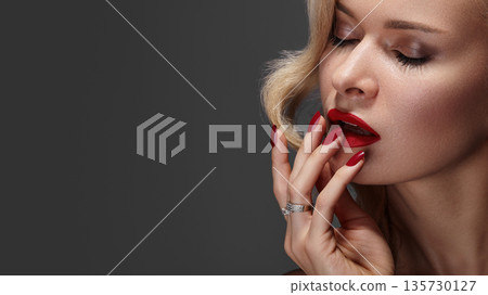 Sexy woman with striking fashion makeup, featuring bright red lips and red nails. Blond curly hairstyle completes glamorous look. Perfect pin-up beauty with bold style Sexy woman with striking fashion makeup, featuring bright red lips and red nails. Blond curly hairstyle completes glamorous look. Perfect pin-up beauty with bold style 135730127