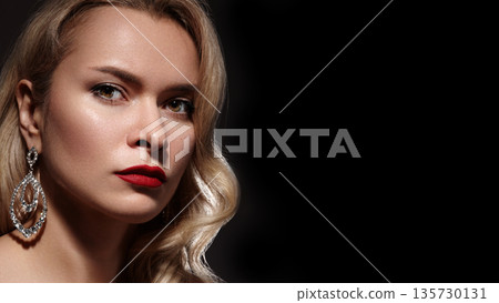Elegant sexy woman sporting fashion makeup and blond curly waves. Bright accessories enhance glamour pin up girl appearance. Red lips paired with sparkling earrings and rings in American diva style Elegant sexy woman sporting fashion makeup and blond curly waves. Bright accessories enhance glamour pin up girl appearance. Red lips paired with sparkling earrings and rings in American diva style 135730131