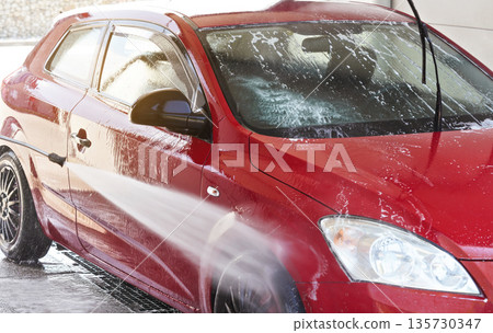 Red car washed in self serve carwash, water spraying to side and front wheel 135730347