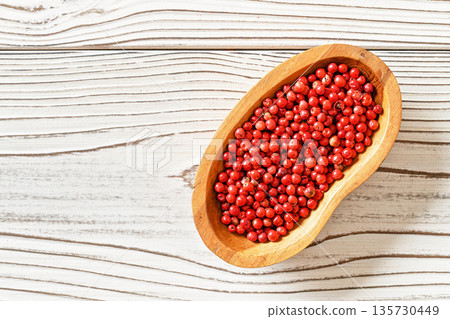 Red or Pink peppercorn in small wooden bowl, on white boards desk, closeup photo from above 135730449