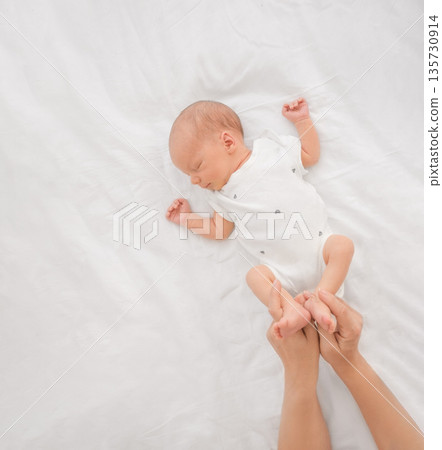 The newborn baby is lying on the bed, sleeping soundly. The mother gently holds her son's legs. A child's restful, sound sleep The newborn baby is lying on the bed, sleeping soundly. The mother gently holds her son's legs. A child's restful, sound sleep 135730914