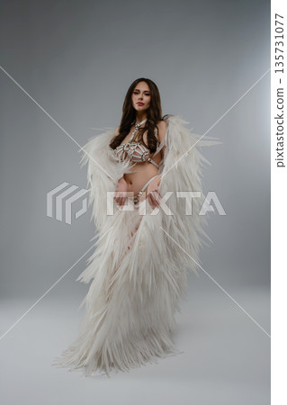 Studio portrait of a woman in a conceptual fantasy costume with white wings and a strappy harness. Studio portrait of a woman in a conceptual fantasy costume with white wings and a strappy harness. 135731077