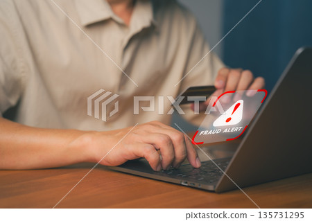 Close-up of hands holding a credit card and typing on a laptop with a Fraud Alert warning. Concept for online scam, cyber security, and credit card fraud prevention. Close-up of hands holding a credit card and typing on a laptop with a Fraud Alert warning. Concept for online scam, cyber security, and credit card fraud prevention. 135731295