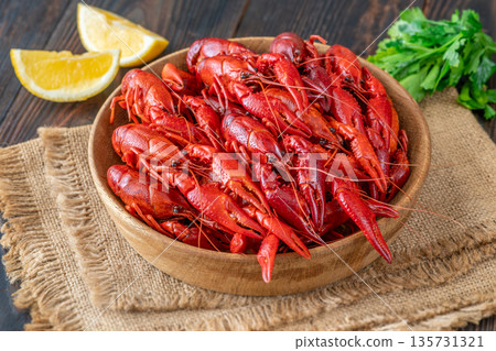 Wooden bowl of bright red boiled crawfish with lemon and parsley, rustic table 135731321