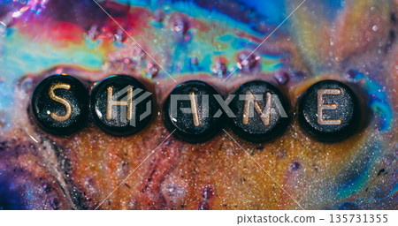 Shine word. Glitter paint. Blur yellow purple orange color sparkling rainbow letters liquid drip mix black texture on abstract bright background. 135731355