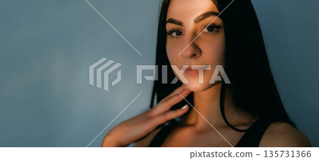 Shiny look. Face flare. Smiling pretty woman in dark touching chin neck radiant skin. Charming cosmetic model in evening light lens. 135731366