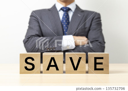 A businessman with his arms crossed and a block with the word "SAVE" written on it A businessman with his arms crossed and a block with the word "SAVE" written on it 135732706