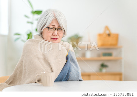 Senior woman feeling cold with a blanket over her shoulders in the living room (chills, cold, immunity) 135733091
