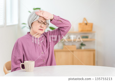 客廳裡，一位頭髮花白的老婦人因發燒而摀著額頭。 135733213