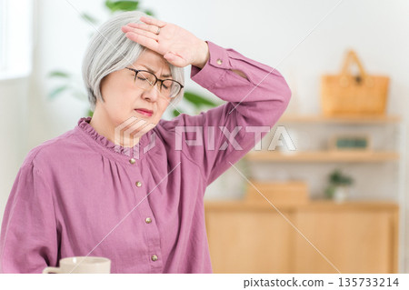 客廳裡，一位頭髮花白的老婦人因發燒而摀著額頭。 135733214