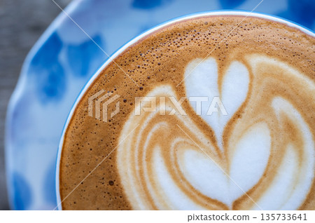 Cropped shot view of the heart on surface of hot latte coffee. A latte is a coffee drink made with espresso and steamed milk. Cropped shot view of the heart on surface of hot latte coffee. A latte is a coffee drink made with espresso and steamed milk. 135733641