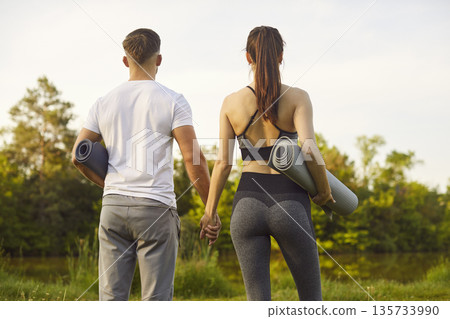 Back view of young sporty couple wearing sportswear holding yoga mat in park before sport workout Back view of young sporty couple wearing sportswear holding yoga mat in park before sport workout 135733990
