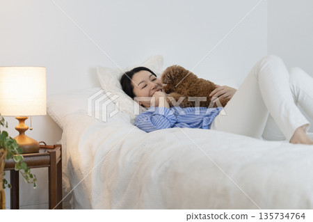 A middle-aged woman hugging her pet dog while lying in bed A middle-aged woman hugging her pet dog while lying in bed 135734764