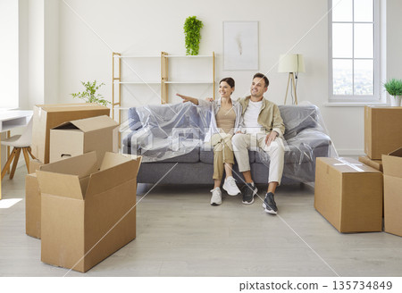 Smiling couple planning new apartment layout while sitting on sofa amid boxes Smiling couple planning new apartment layout while sitting on sofa amid boxes 135734849