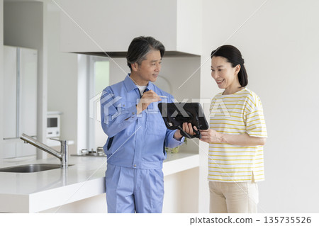 一位中年婦女正在聽一位承包商拿著平板電腦解釋。 135735526