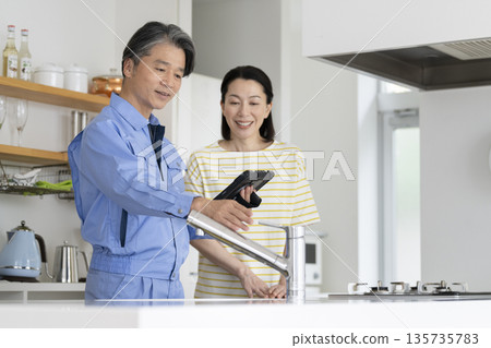 一位中年婦女正在聽承包商檢查廚房管道並進行解說。 135735783