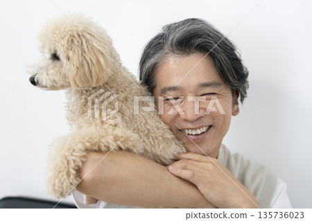 一位五十多歲的男士面帶微笑,抱著他心愛的狗狗。這是與狗狗共度美好時光的畫面。 一位五十多歲的男士面帶微笑,抱著他心愛的狗狗。這是與狗狗共度美好時光的畫面。 135736023