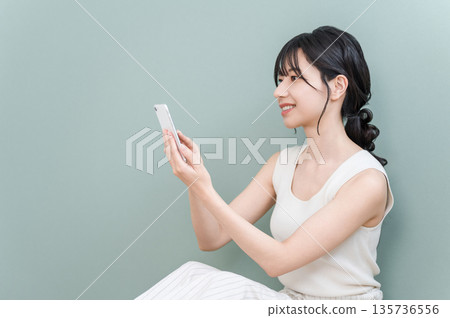Smiling Asian woman using smartphone at home (app, matching app) 135736556