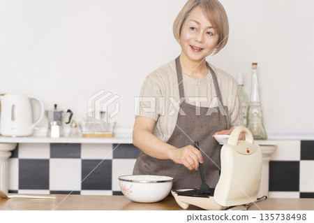 一位老婦人在廚房裡烤美式華夫餅 一位老婦人在廚房裡烤美式華夫餅 135738498