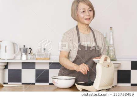 Senior woman baking American waffles in the kitchen 135738499