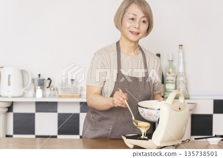 Senior woman baking American waffles in the kitchen Senior woman baking American waffles in the kitchen 135738501