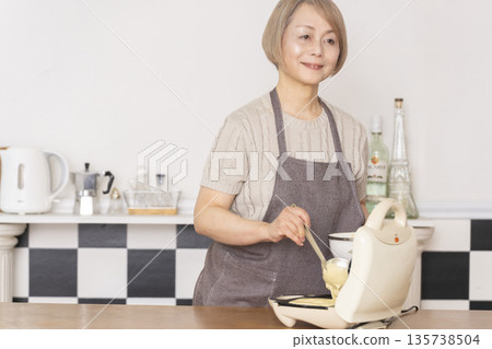 Senior woman baking American waffles in the kitchen Senior woman baking American waffles in the kitchen 135738504