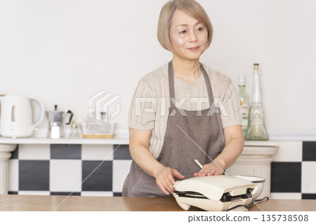 Senior woman baking American waffles in the kitchen Senior woman baking American waffles in the kitchen 135738508
