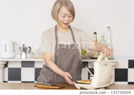 一位老婦人在廚房裡烤美式華夫餅 135738509