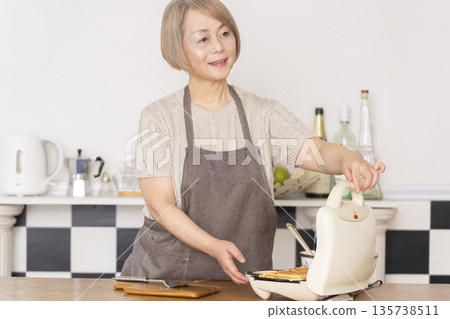 Senior woman baking American waffles in the kitchen Senior woman baking American waffles in the kitchen 135738511