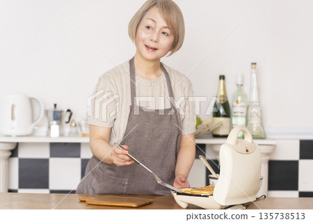 Senior woman baking American waffles in the kitchen Senior woman baking American waffles in the kitchen 135738513