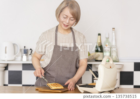 Senior woman baking American waffles in the kitchen Senior woman baking American waffles in the kitchen 135738515