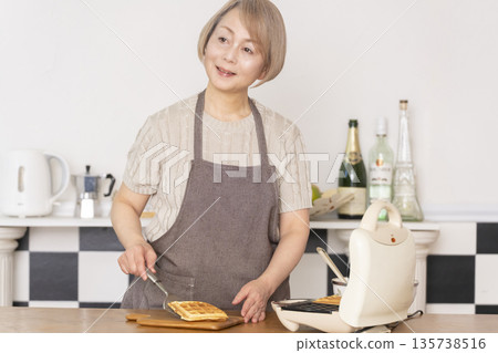 Senior woman baking American waffles in the kitchen Senior woman baking American waffles in the kitchen 135738516