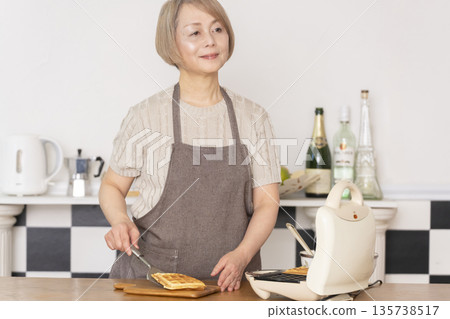 Senior woman baking American waffles in the kitchen Senior woman baking American waffles in the kitchen 135738517