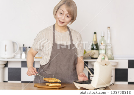 一位老婦人在廚房裡烤美式華夫餅 一位老婦人在廚房裡烤美式華夫餅 135738518