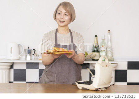 一位老婦人在廚房裡烤美式華夫餅 一位老婦人在廚房裡烤美式華夫餅 135738525
