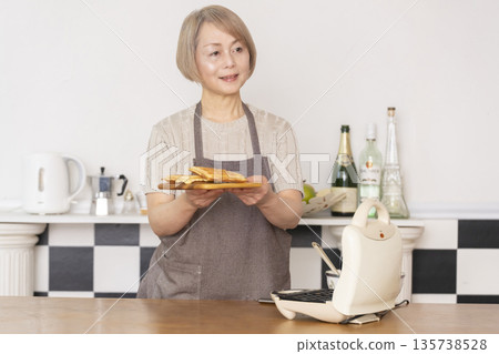 一位老婦人在廚房裡烤美式華夫餅 一位老婦人在廚房裡烤美式華夫餅 135738528