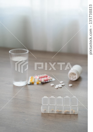 Flat lay of medicines with water glass and pill organizer on table, daily medication schedule, healthcare treatment, dosage planning, copy space background. Flat lay of medicines with water glass and pill organizer on table, daily medication schedule, healthcare treatment, dosage planning, copy space background. 135738833
