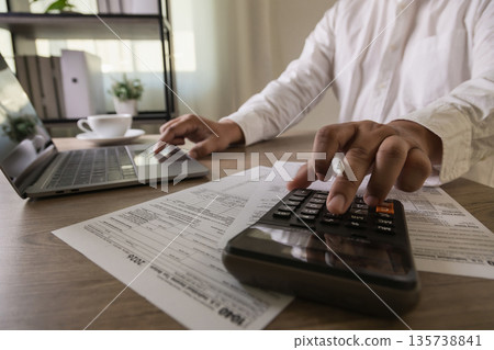 Income tax return preparation with calculator 1040 forms, businessman working on laptop to calculate deductions, manage expenses, plan budget for tax season, tax reduction Income tax return preparation with calculator 1040 forms, businessman working on laptop to calculate deductions, manage expenses, plan budget for tax season, tax reduction 135738841