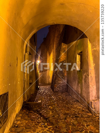 Street in the city at night with light shining through an archway Street in the city at night with light shining through an archway 135739220