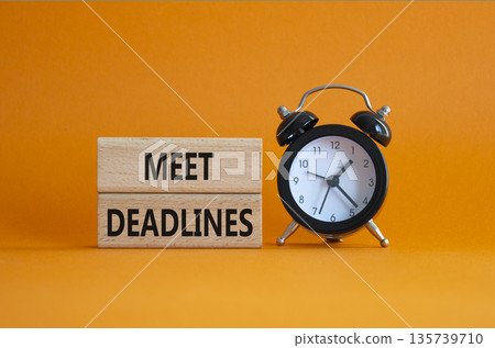 Meet Deadlines symbol. Concept word Meet Deadlines on wooden blocks. Beautiful orange background with alarm clock. Business and Meet Deadlines concept. Copy space Meet Deadlines symbol. Concept word Meet Deadlines on wooden blocks. Beautiful orange background with alarm clock. Business and Meet Deadlines concept. Copy space 135739710