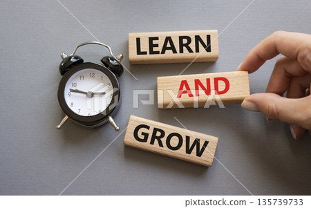 Learn and grow symbol. Concept words Learn and grow on wooden blocks. Businessman hand. Beautiful grey background with alarm clock. Business and Learn and grow concept. Copy space. 135739733