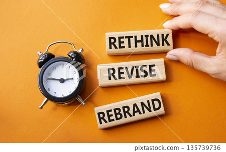 Rethink Revise Rebrand symbol. Wooden blocks with words Rethink Revise Rebrand. Businessman hand. Beautiful orange background with alarm clock. Business and Rethink Revise Rebrand concept. Copy space. 135739736